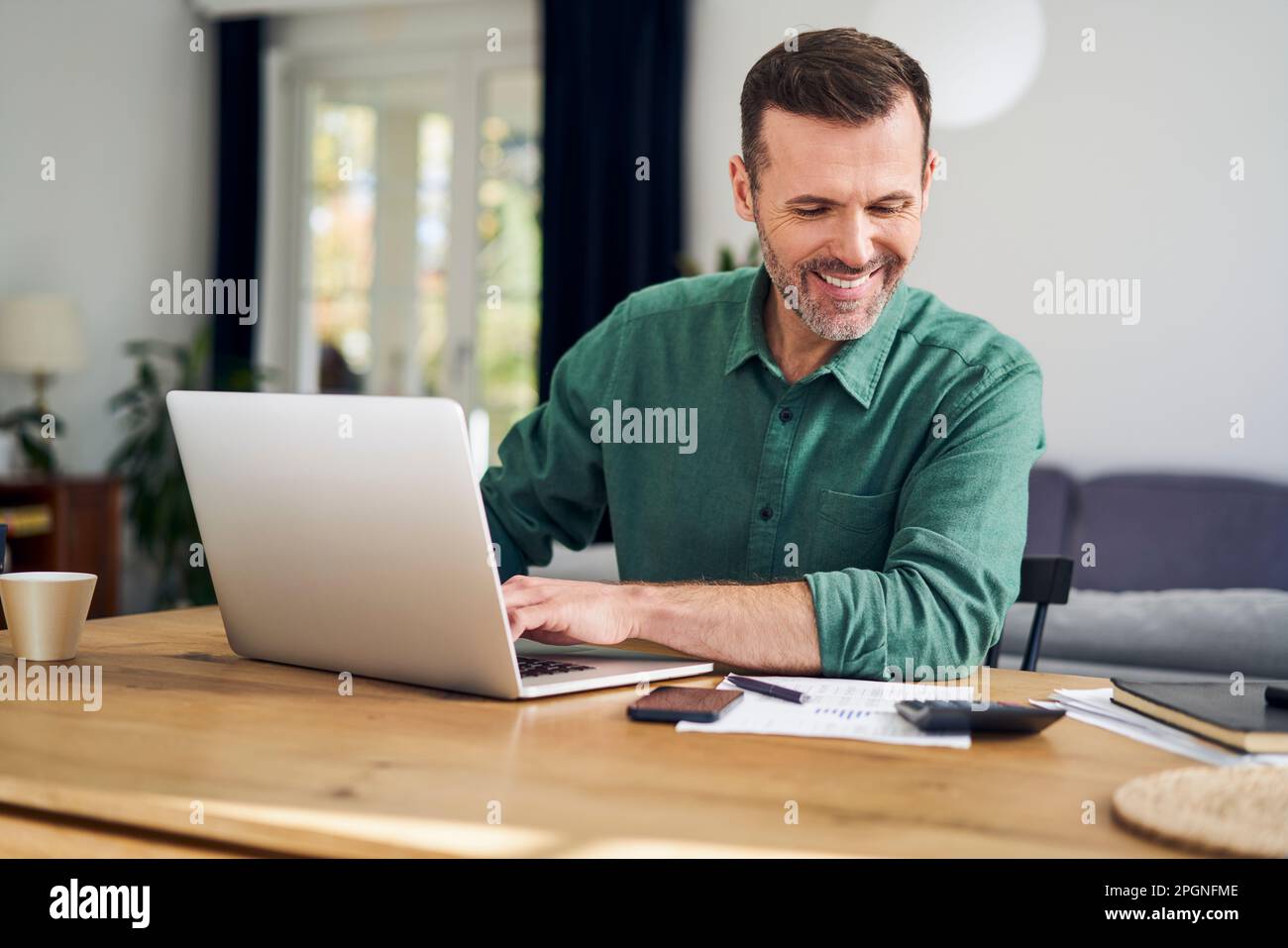 Katowice, Silésie, Pologne. Un homme d'âge moyen heureux qui travaille sur un ordinateur portable pour calculer les finances de la maison Banque D'Images