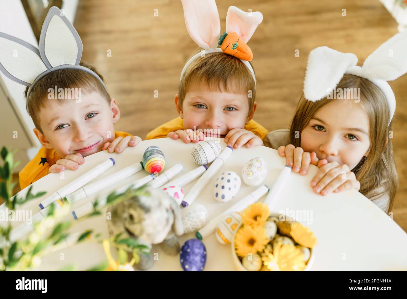 Des frères et sœurs souriants portant des oreilles de lapin près de la table à la maison Banque D'Images