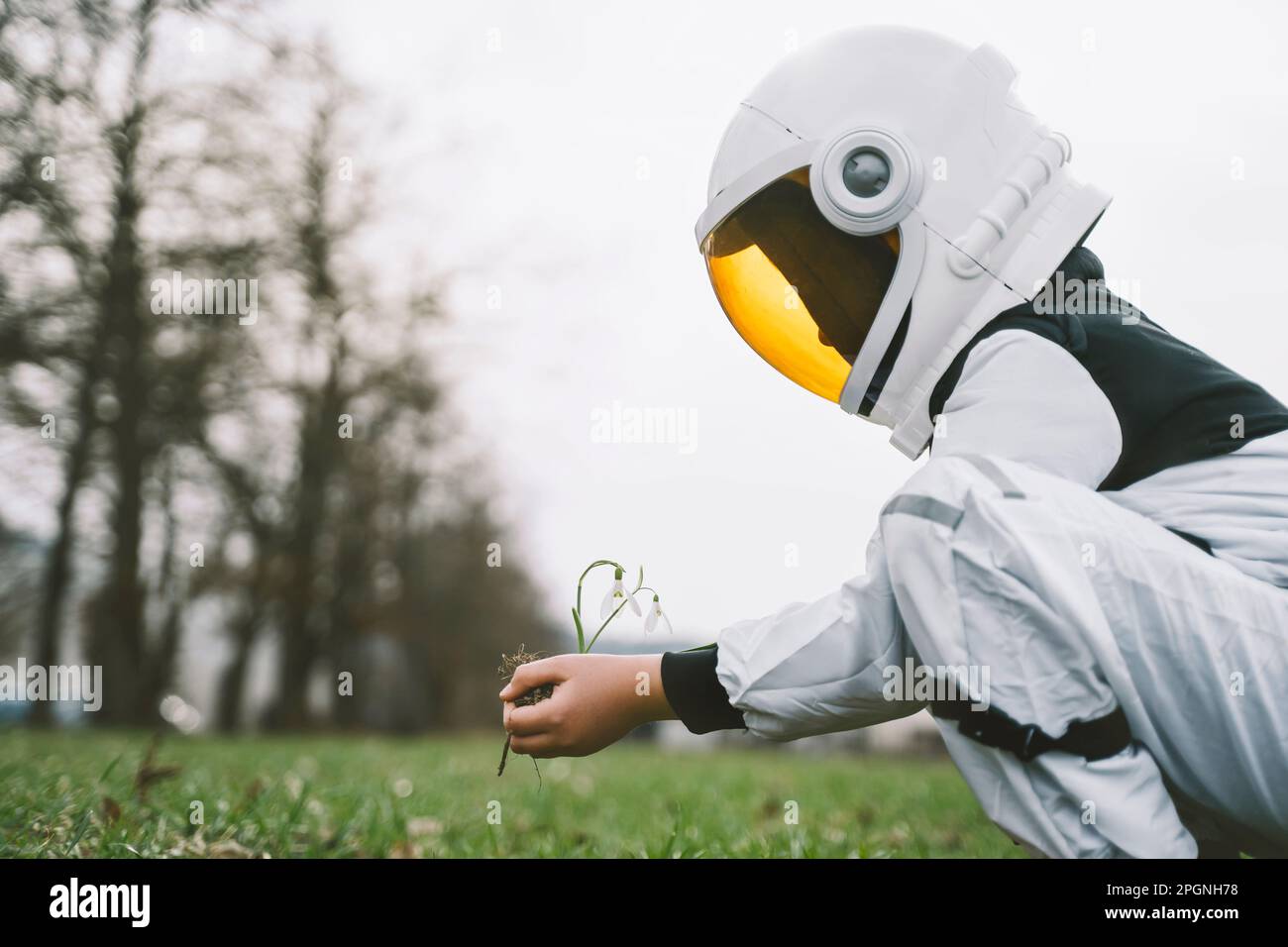 Garçon portant le costume d'astronaute ramassant une plante florale dans la nature Banque D'Images