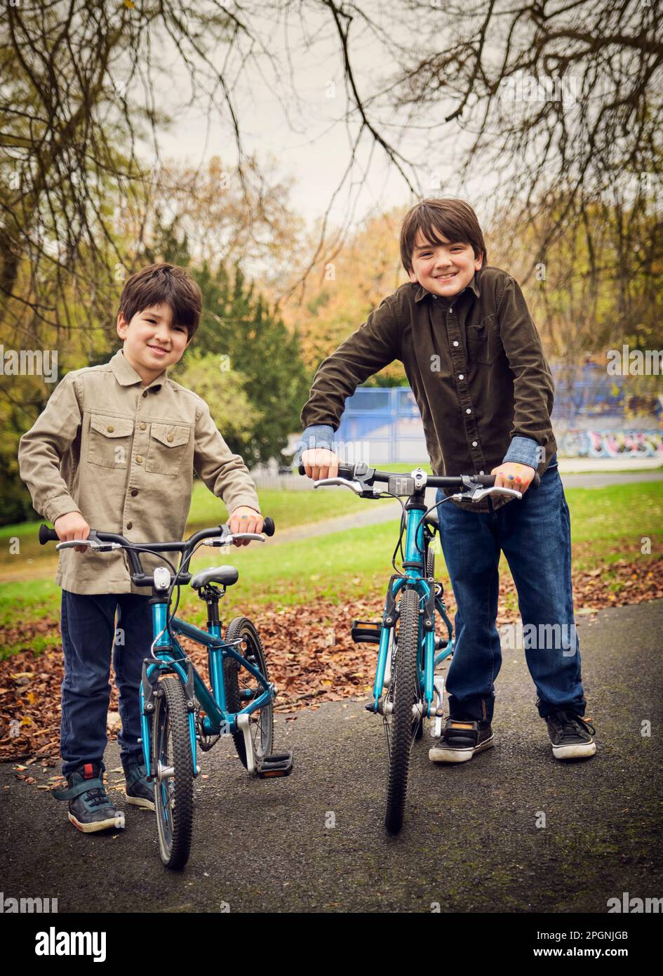 Frères souriants avec des vélos debout sur la piste de marche au parc Banque D'Images