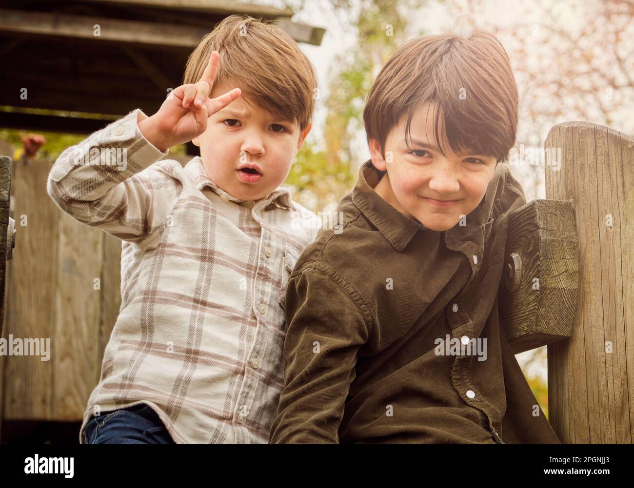 Un garçon faisant signe de paix par un frère jouant au parc Banque D'Images