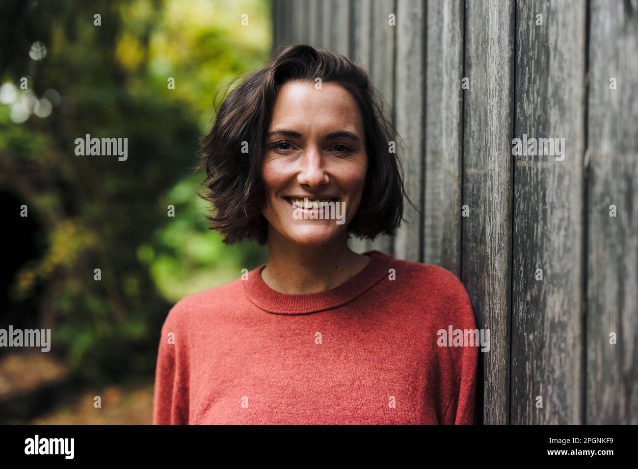 Femme souriante avec des cheveux foncés penchés sur le mur Banque D'Images