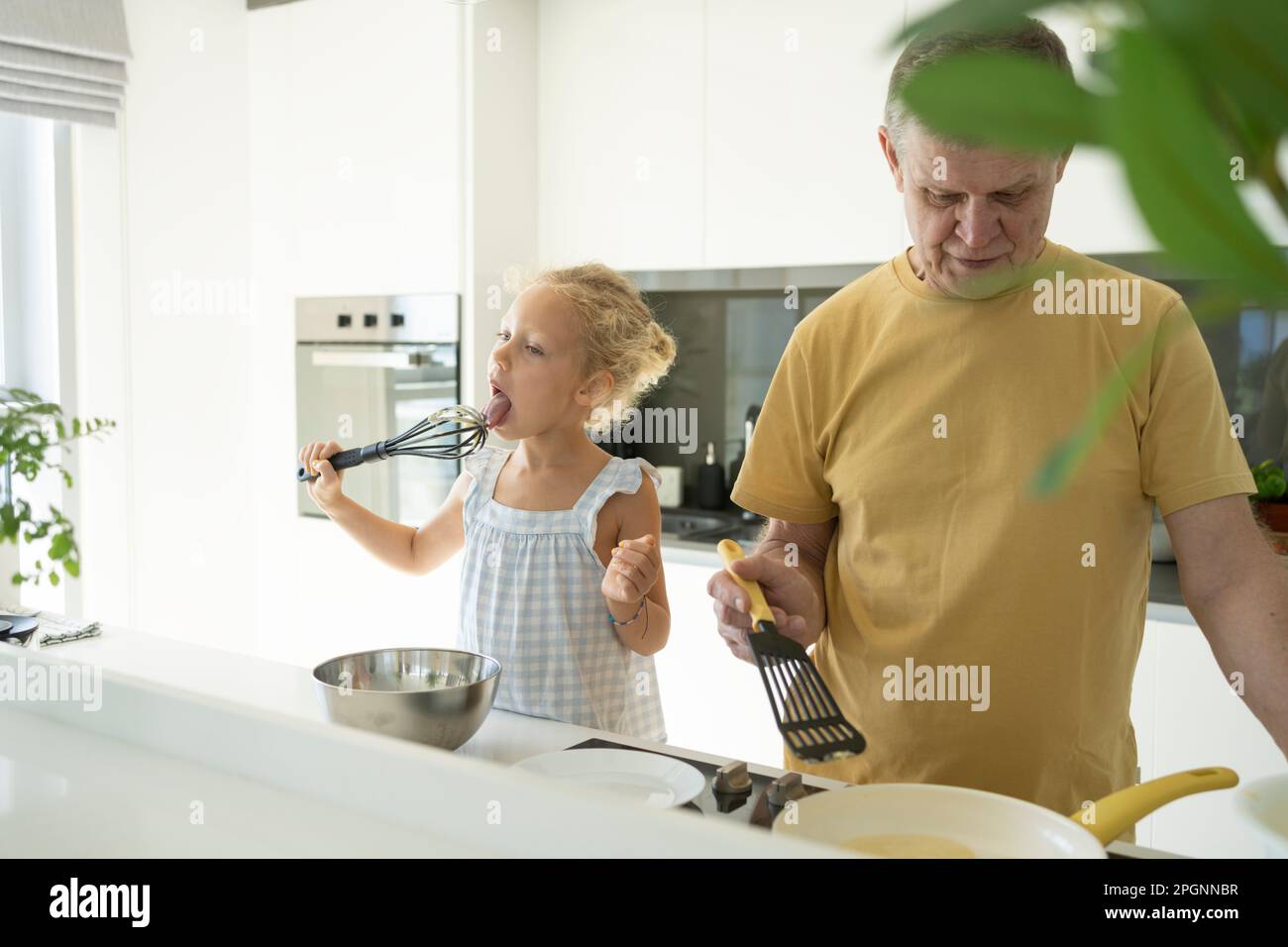 Tire-paille d'oeufs de lécking de fille par grand-père préparant la nourriture dans la cuisine Banque D'Images