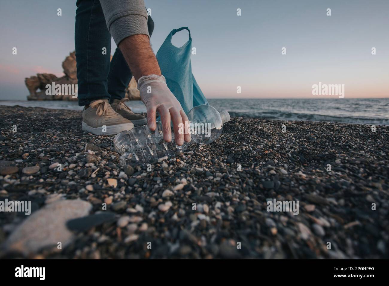 Main de l'homme ramassant une bouteille en plastique sur la plage Banque D'Images