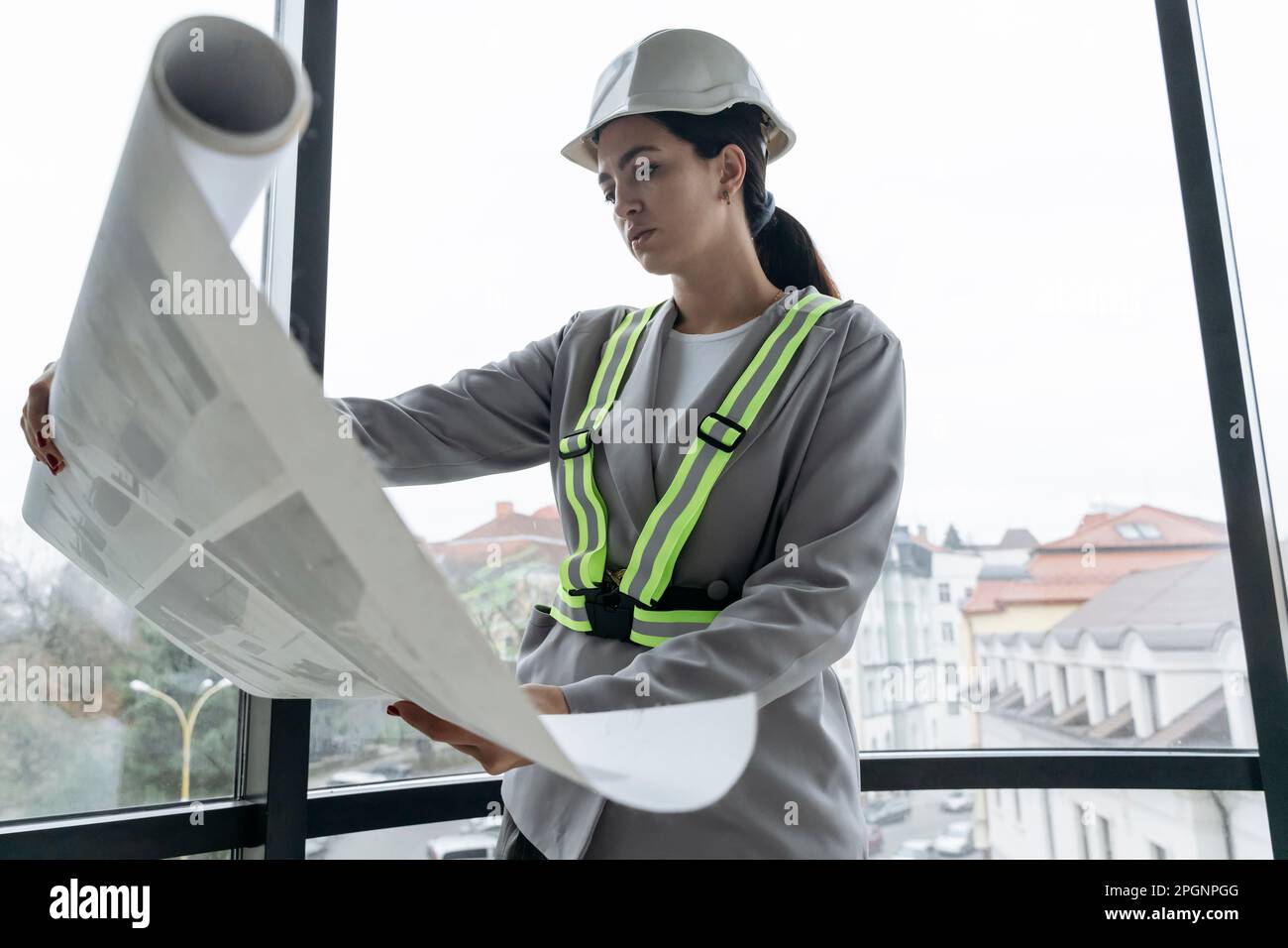 Architecte portant un plan de lecture de casque de sécurité devant la fenêtre du bureau Banque D'Images