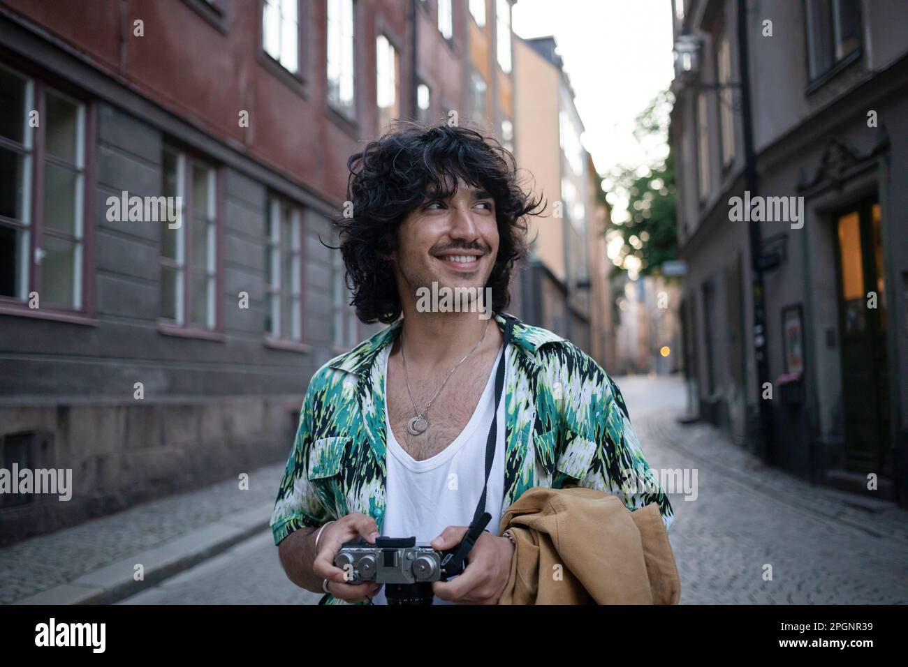 Homme souriant debout avec un appareil photo au milieu des bâtiments Banque D'Images