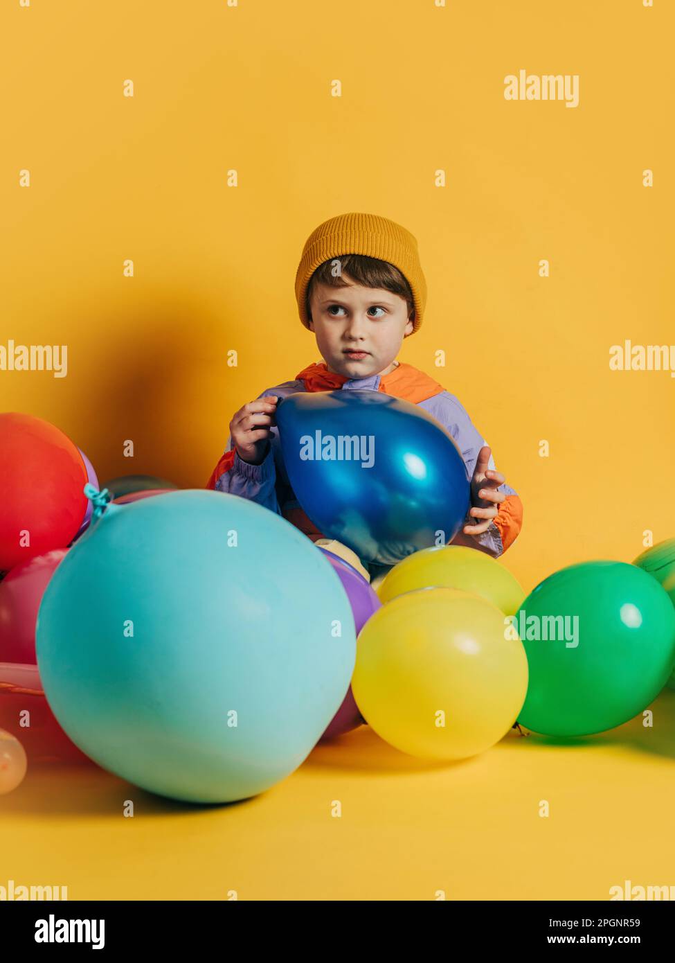 Garçon assis avec des ballons multicolores sur fond jaune Banque D'Images