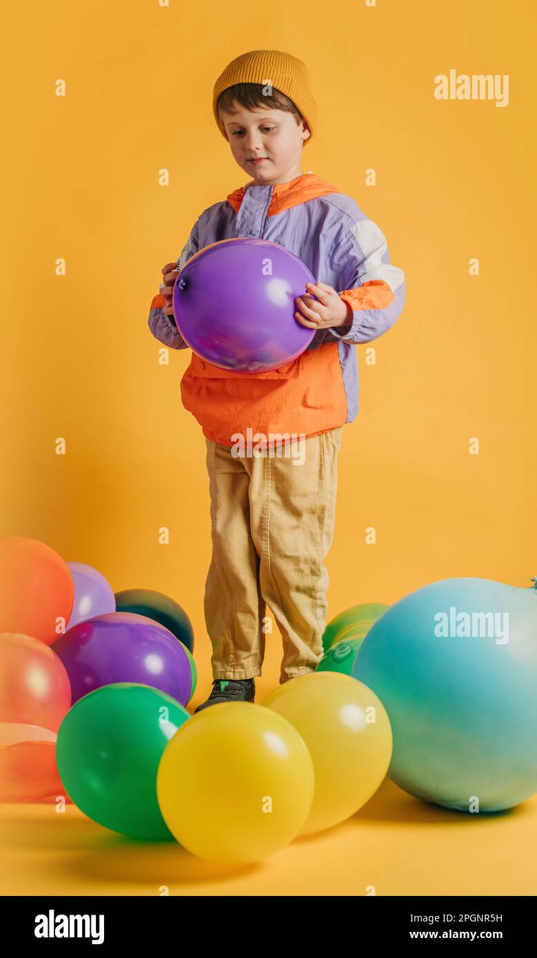 Garçon jouant avec des ballons multicolores sur fond jaune Banque D'Images