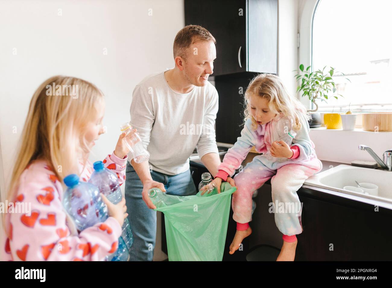 Père souriant recyclant des bouteilles en plastique avec des filles à la maison Banque D'Images