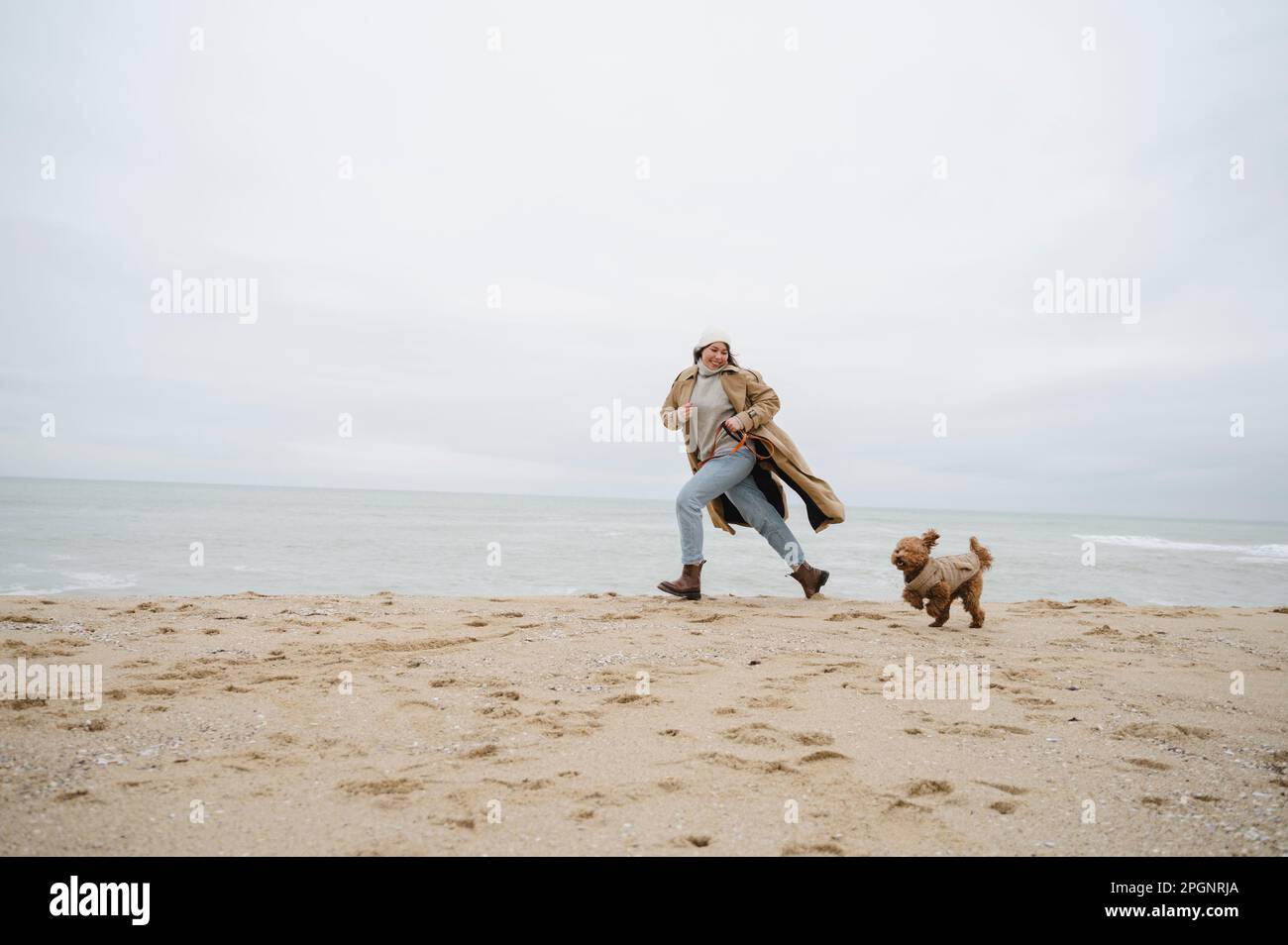 Femme en train de courir avec un chien sur le sable à la plage Banque D'Images