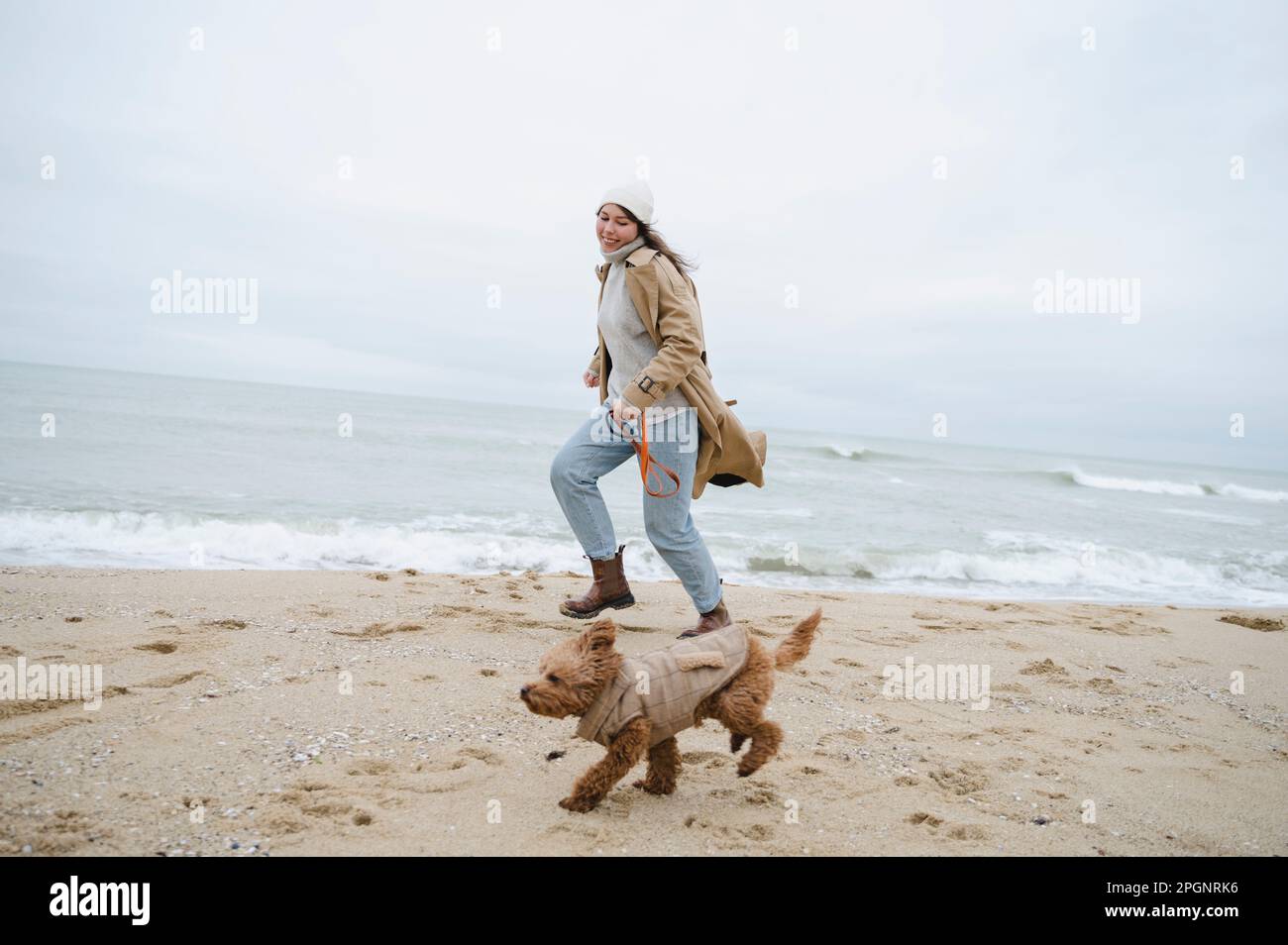 Femme en train de courir avec un chien près du rivage à la plage Banque D'Images