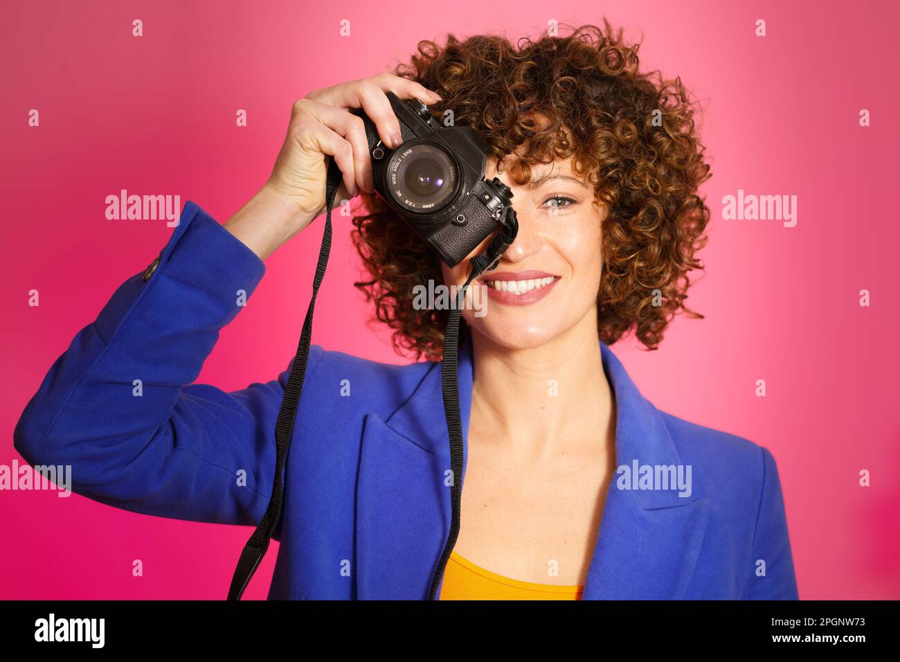 Femme souriante photographiant avec l'appareil photo sur fond magenta Banque D'Images