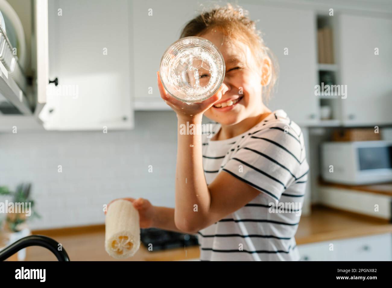 Une fille ludique lavant des plats avec loofah à la maison Banque D'Images