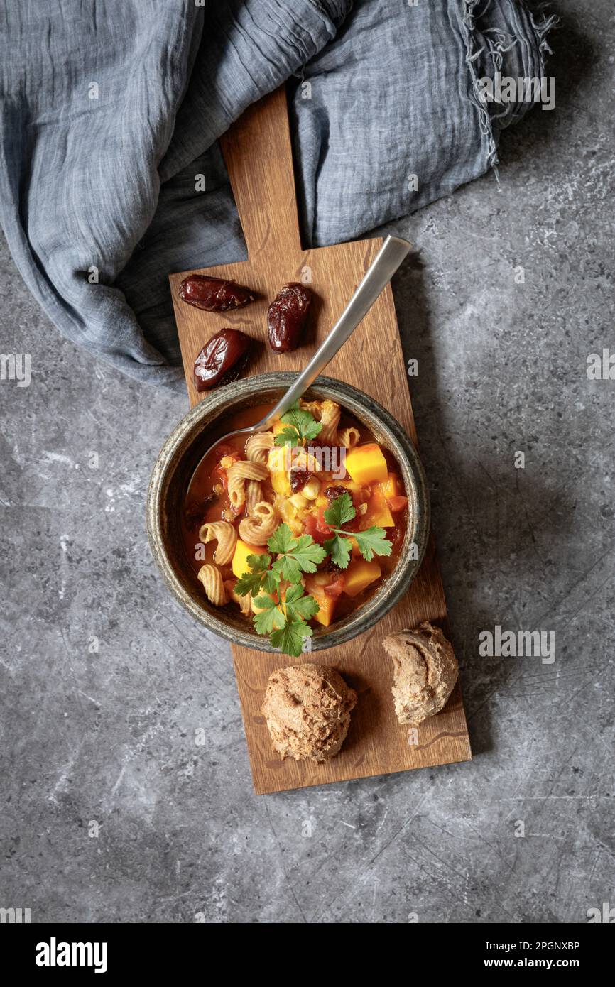 Photo studio d'un bol de ragoût nord-africain prêt à manger avec potiron, pois chiches, lentilles, dattes et coriandre Banque D'Images