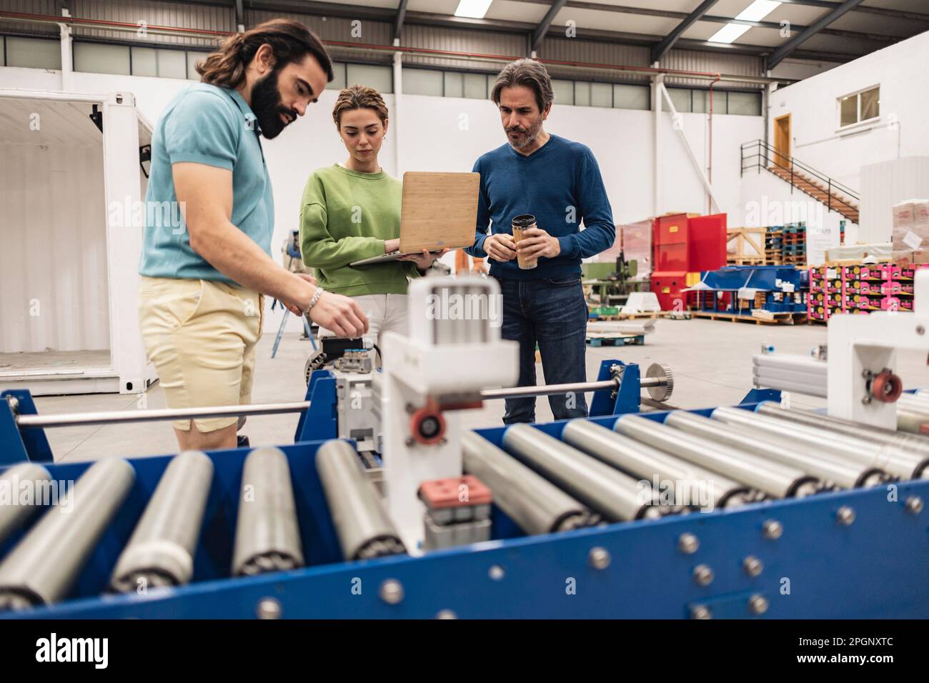 Les ingénieurs analysent les pièces de la machine avec le tapis convoyeur en premier plan Banque D'Images