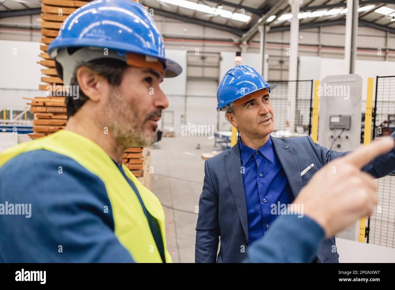Des ingénieurs matures portant un casque de sécurité ayant des discussions dans une usine de robotique Banque D'Images