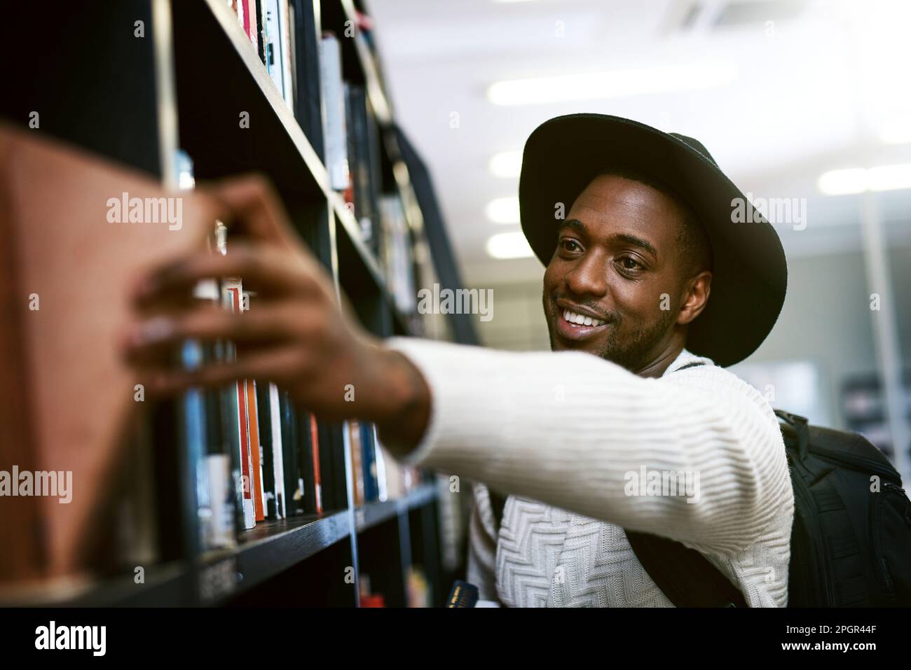 Fiction ou non fiction, hes un fan des deux. un jeune homme heureux de retirer un livre d'une étagère dans une bibliothèque d'université. Banque D'Images