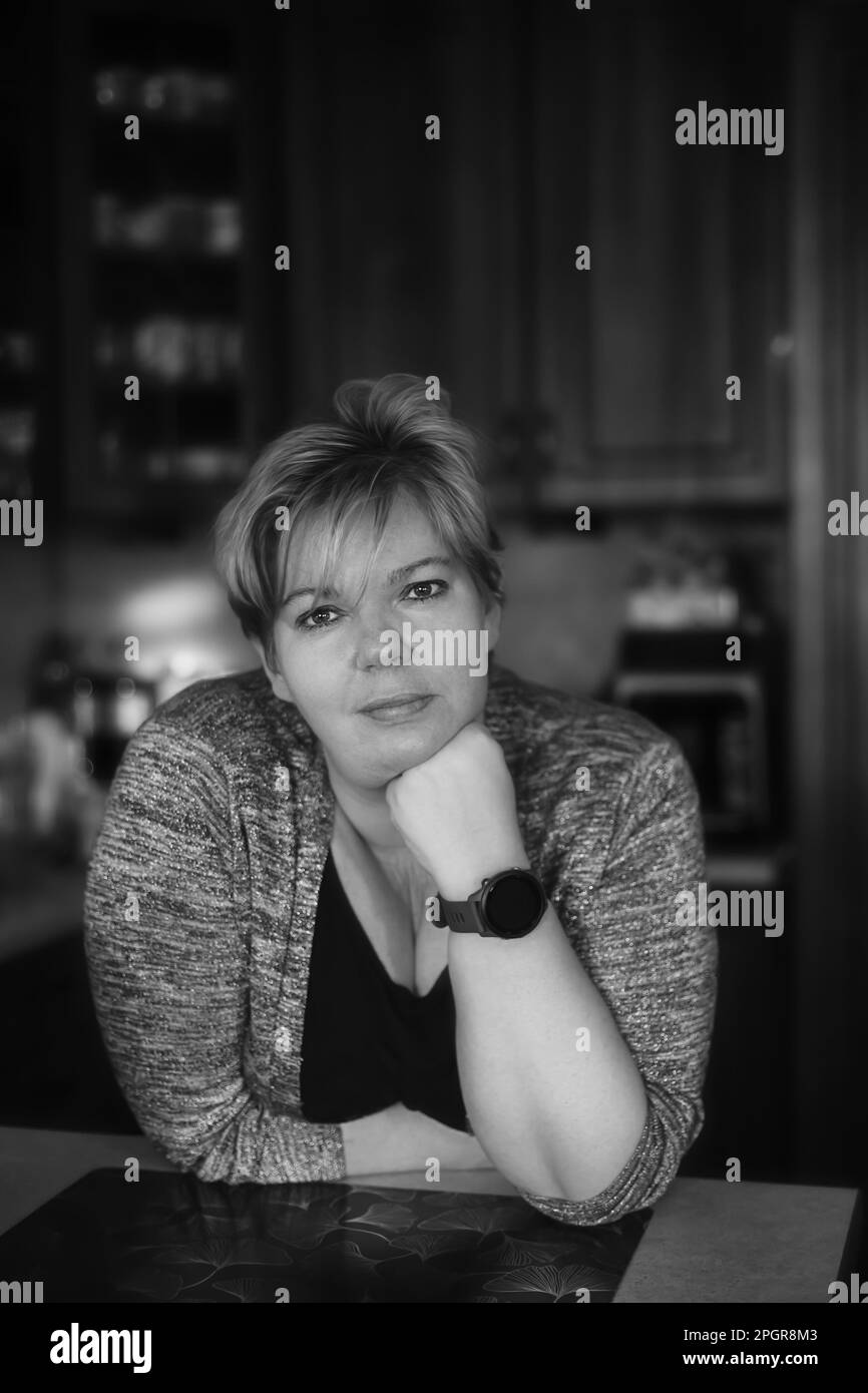 Portrait noir et blanc d'une belle femme mûre penchée contre un comptoir de cuisine Banque D'Images