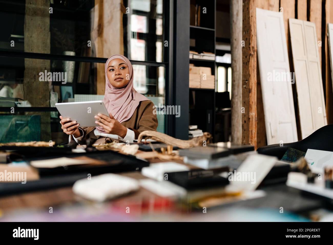 Une femme arabe pensive designer portant le hijab travaillant sur une tablette à l'atelier Banque D'Images