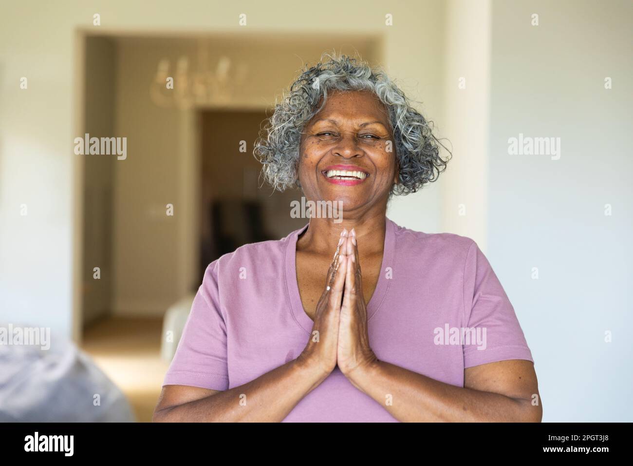 Une femme afro-américaine joyeuse souriante et méditant dans la pose de prière à la maison, l'espace de copie. Portrait, non modifié, style de vie, retraite, yoga, ex Banque D'Images