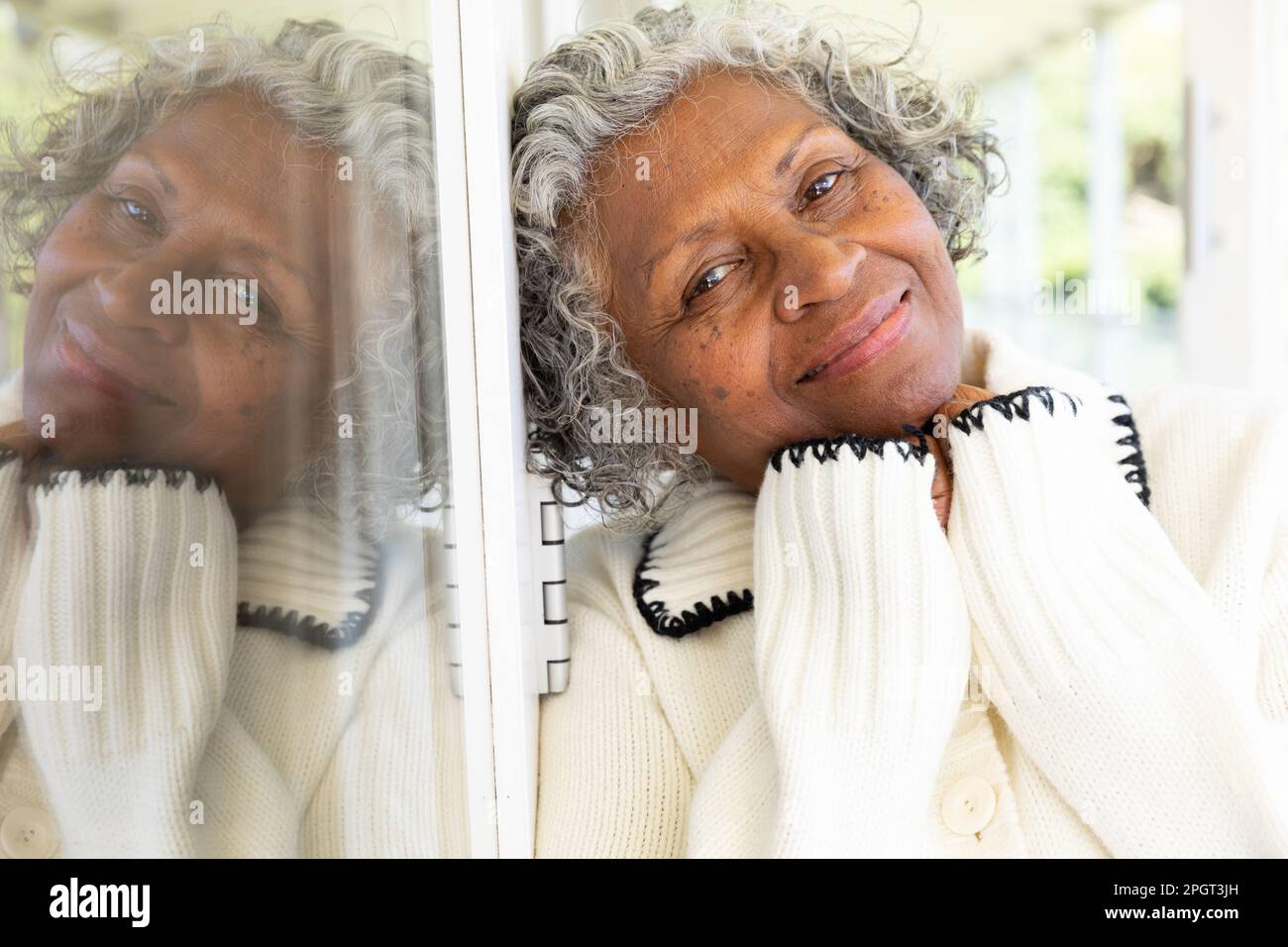 Gros plan d'une femme afro-américaine souriante avec les mains sur le menton penchées sur la fenêtre du balcon. Non modifié, style de vie, portrait, réflexion et retraité Banque D'Images