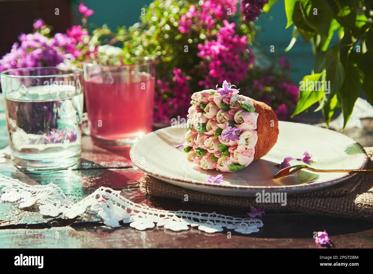 Table extérieure de printemps avec l'esthétique florale cupcake, compote et verre d'eau. Fleurs de lilas printanières en plein air par beau temps. Créateur desserts rêveux co Banque D'Images
