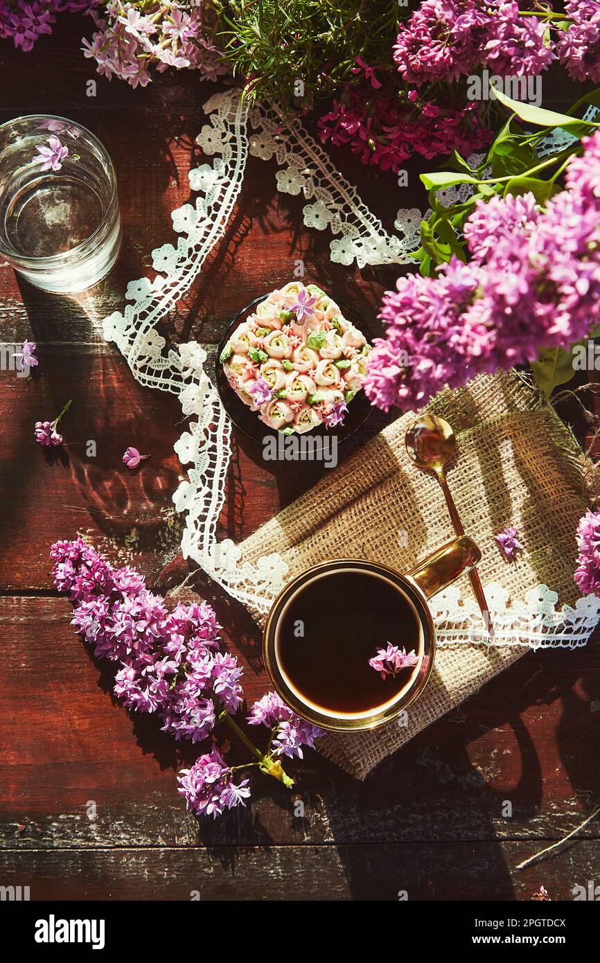 Table de printemps esthétique avec cupcake floral rose, fleurs lilas, tasse de café sous les ombres dures couché plat Banque D'Images
