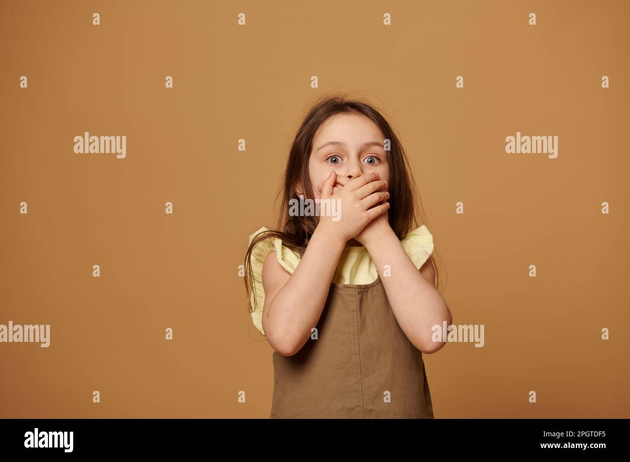 Une petite petite fille effrayée couvre sa bouche avec les mains. Droits des enfants. Peurs de l'enfance. Concept de protection de l'enfant Banque D'Images