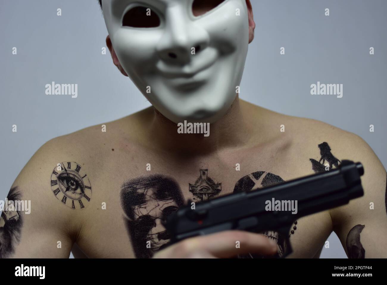 Un homme portant un masque facial, avec de nombreux tatouages visibles, tenant un fusil dans un geste menaçant Banque D'Images