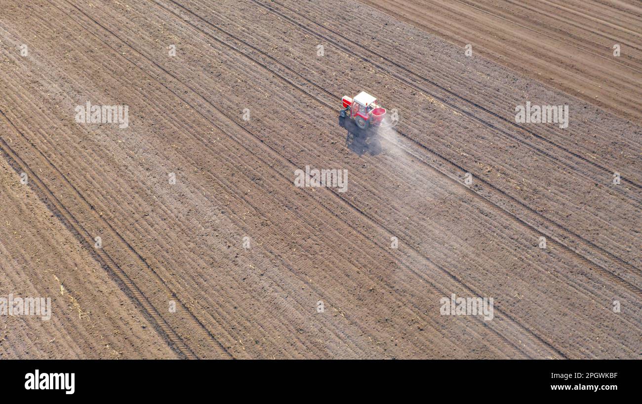 Vue ci-dessus sur le tracteur comme des lancers, fertilisant les terres arables pour de nouvelles récoltes, traînant la machine agricole montée pour l'épandage d'engrais artificiel. Banque D'Images