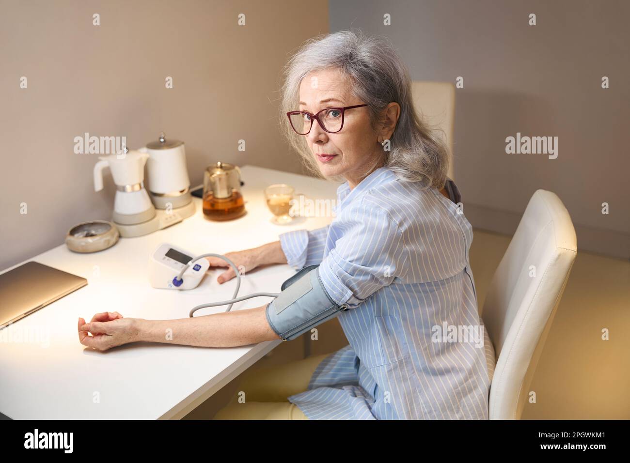 Une jolie femme âgée mesure sa tension artérielle avec un tonomètre Banque D'Images
