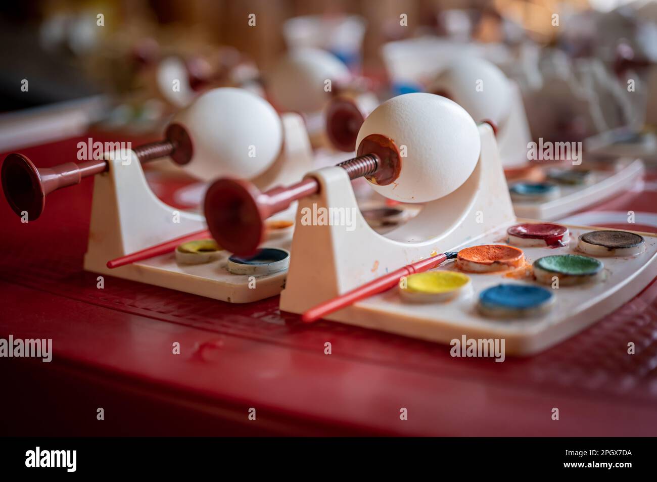 Œufs de Pâques blancs à la maison avec outils de peinture aquarelle sur table rouge. Décoration faite main aux œufs de Pâques. Banque D'Images