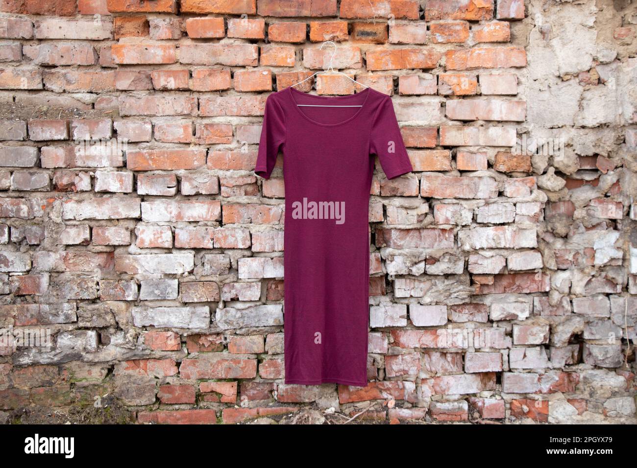 robe rouge pour femmes accrochée sur un vieux mur de briques à l'extérieur au soleil Banque D'Images