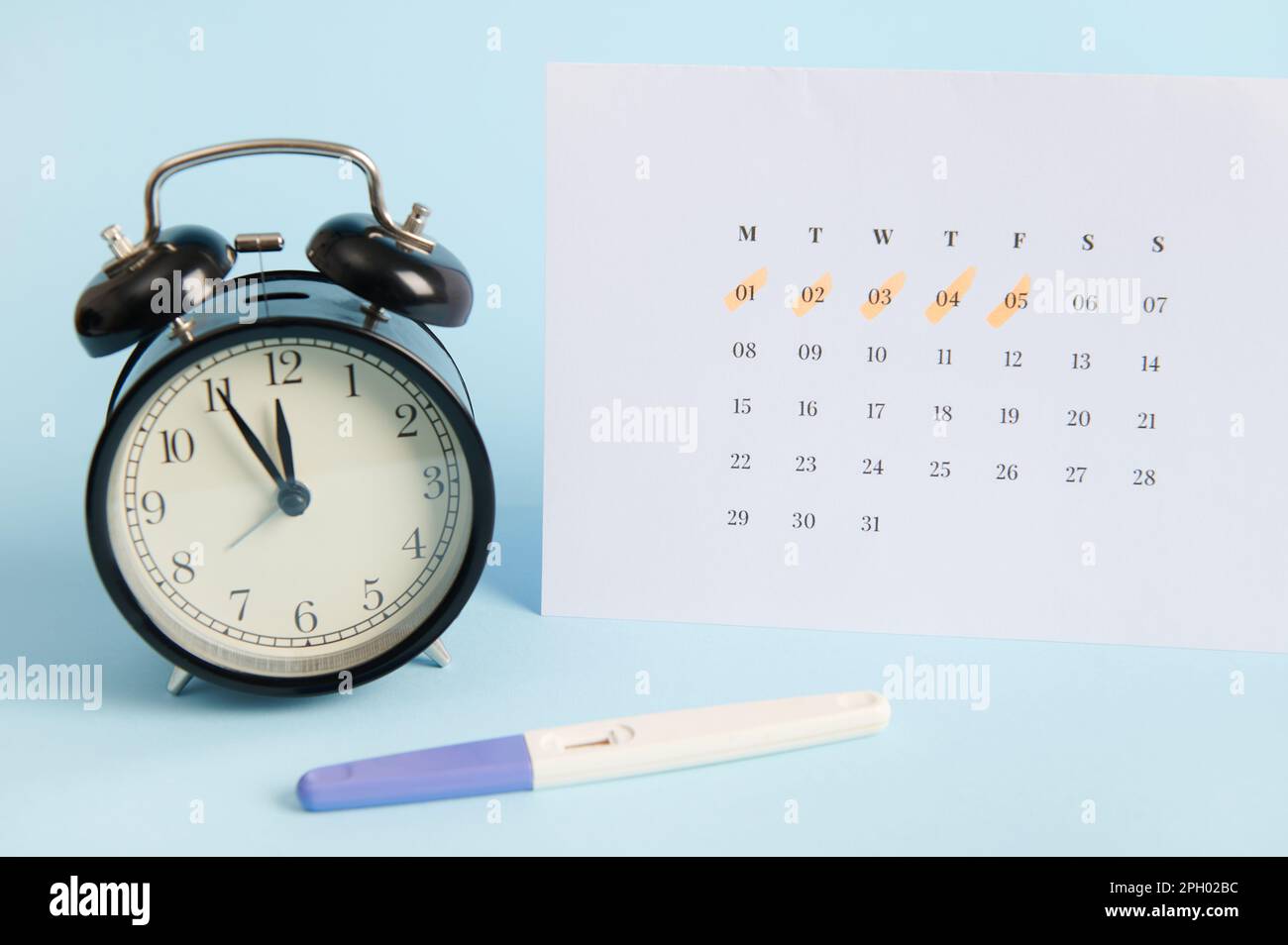 Test de grossesse positif, réveil et calendrier blanc avec les dates de la dernière menstruation marquées sur fond bleu Banque D'Images