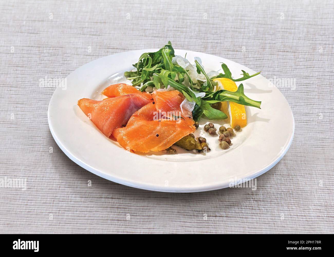 Carpaccio de saumon avec arugula, citron, concombre mariné et câpres sur plaque blanche Banque D'Images