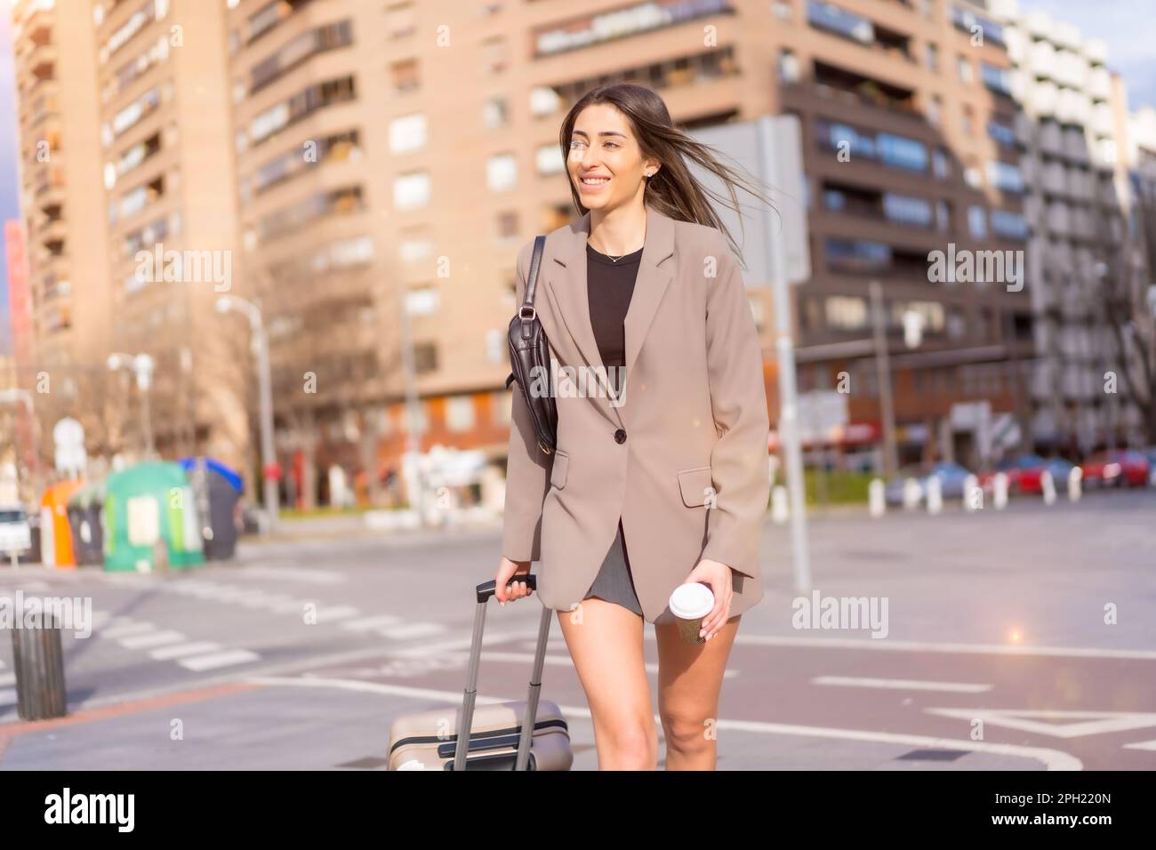 Une jolie femme caucasienne sous un manteau portant une valise et marchant  dans un paysage urbain animé Photo Stock - Alamy