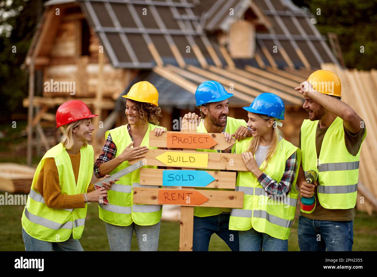 Un groupe de jeunes bâtisseurs gais, tant féminins que masculins, aiment poser pour une photo sur un site de construction de chalet lors d'une belle journée. Construction, buil Banque D'Images