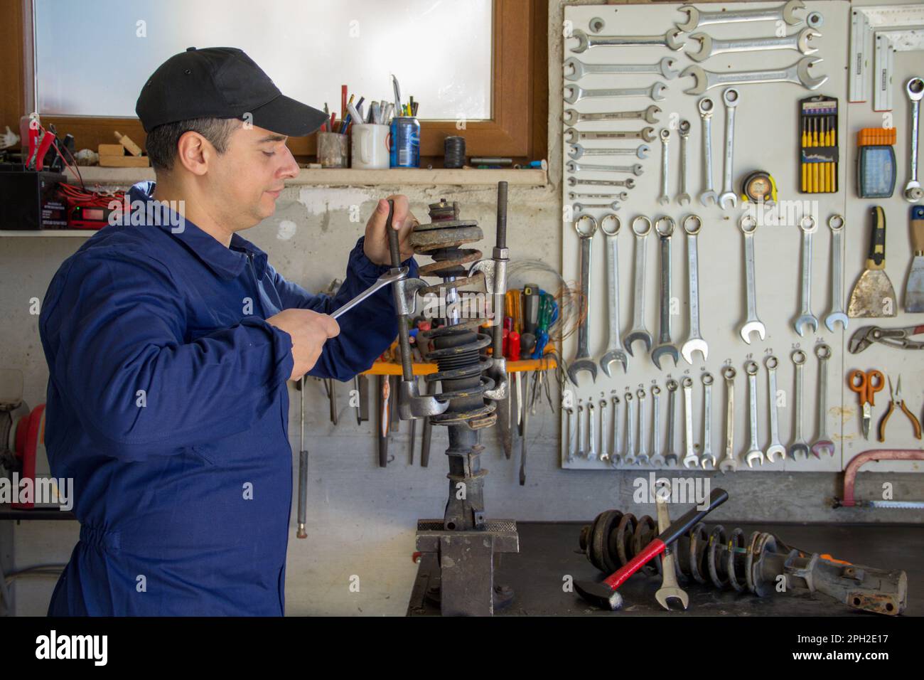 Image d'un mécanicien en combinaison dans son atelier pendant qu'il démonte un amortisseur de voiture avec une clé et des extracteurs. Banque D'Images