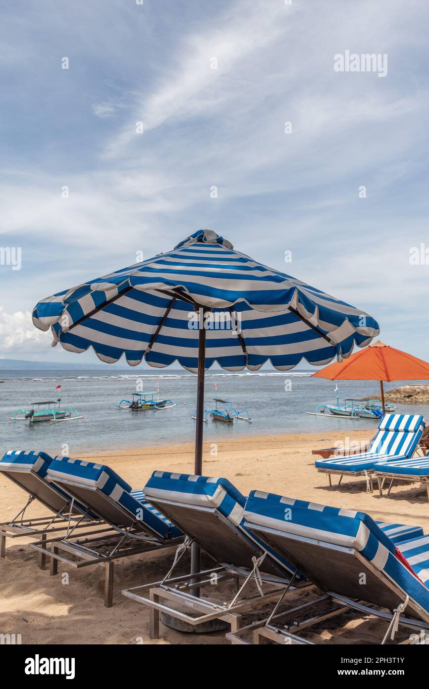 Parasols de plage bleus et blancs à la plage de Sanur. Océan, bateaux, chaises longues, ciel bleu. Bali, Indonésie. Banque D'Images