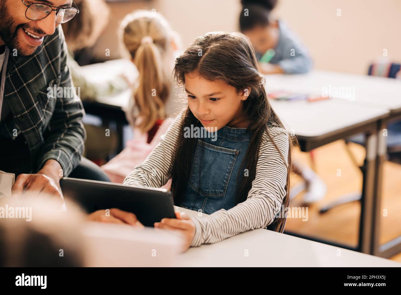 Un enseignant montre à un étudiant comment utiliser une tablette numérique dans une école primaire. Un tuteur masculin enseigne l'alphabétisation numérique et le codage aux jeunes enfants. Enfant e Banque D'Images