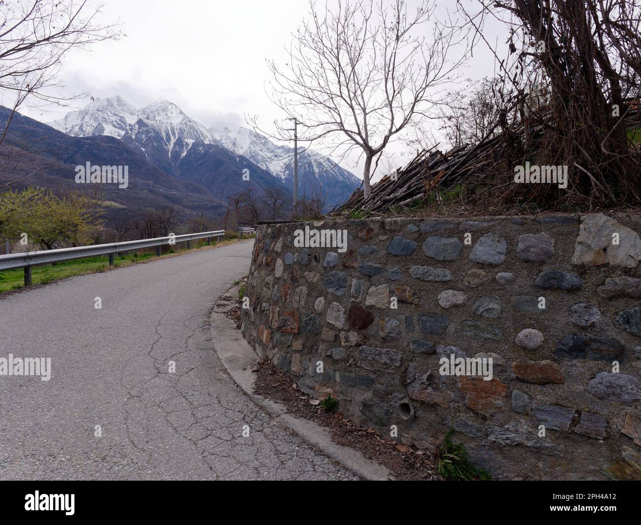 Route surélevée dans nus dans l'Aoste Vallet Italie avec mur en pierre sur la droite et les Alpes enneigées derrière. Banque D'Images