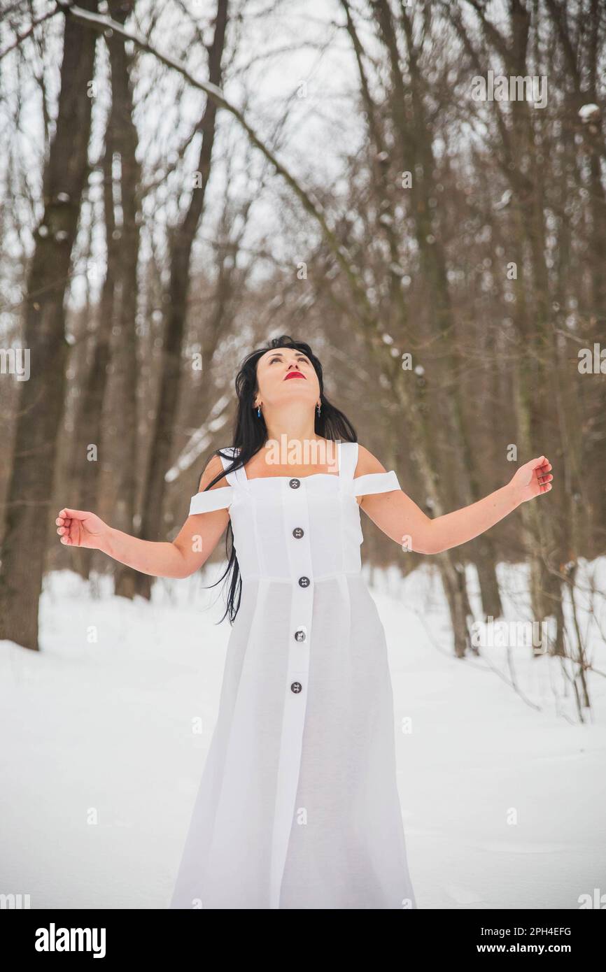 Belle femme en robe blanche priant dans la forêt d'hiver Banque D'Images