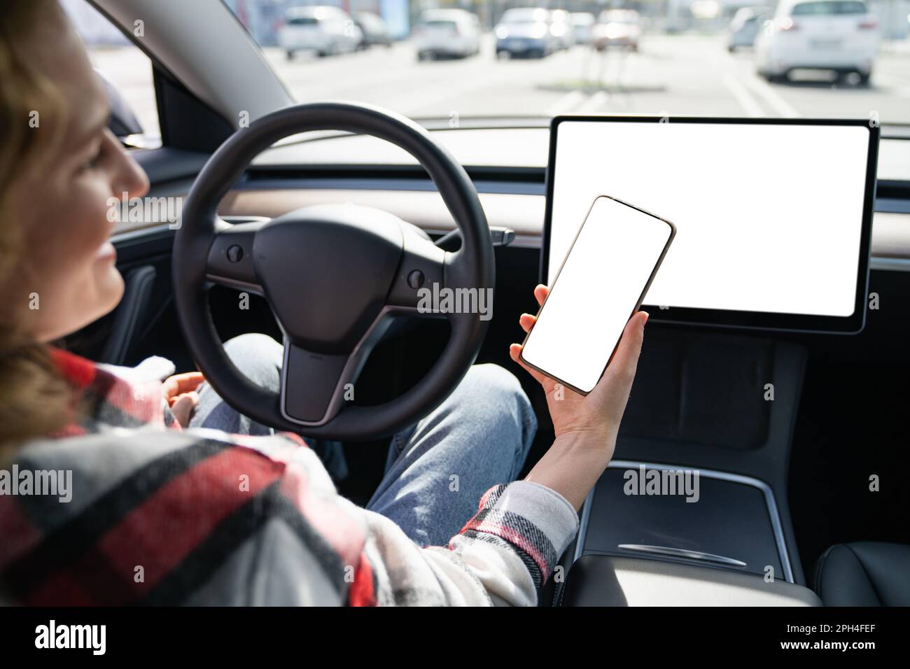 Une femme pilote dans une voiture tient un smartphone avec un écran blanc. Photo de haute qualité Banque D'Images