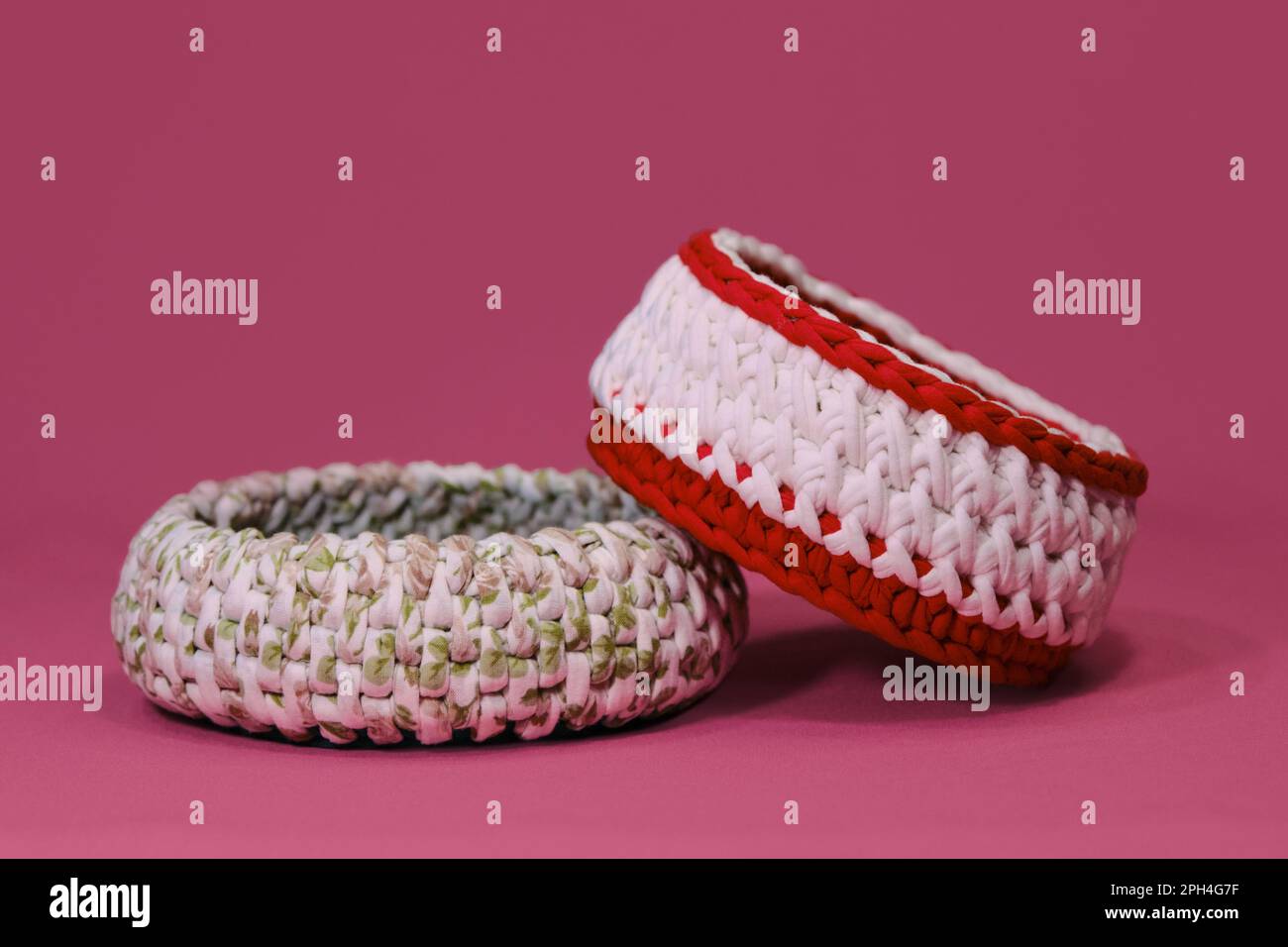 Deux paniers en maille faits maison sur fond rose. Boîtes rondes vertes, rouges et blanches pour petites choses faites de fil crocheté, d'art fait à la main Banque D'Images