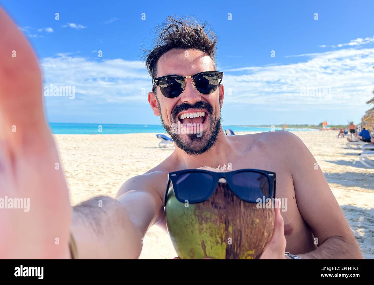 Un homme aime ses vacances luxueuses dans un complexe des Maldives comme il prend un selfie avec une noix de coco et des lunettes de soleil. Le magnifique fond tropical se fixe Banque D'Images