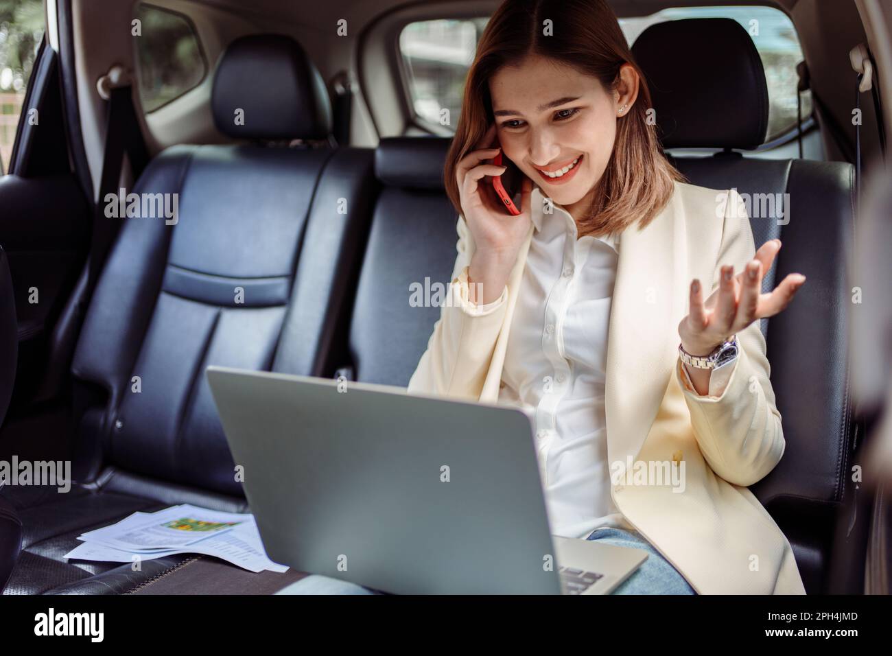 Femme d'affaires parlant sur le téléphone mobile et utilisant l'ordinateur portable dans la voiture. Banque D'Images