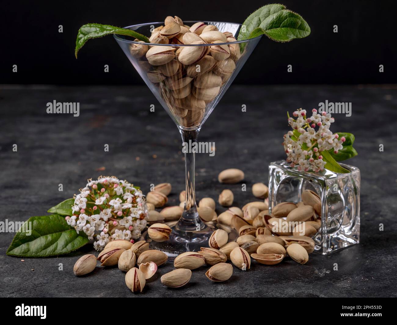 Les pistaches sont contenues dans un verre transparent et placées sur la table, avec des fleurs printanières Banque D'Images