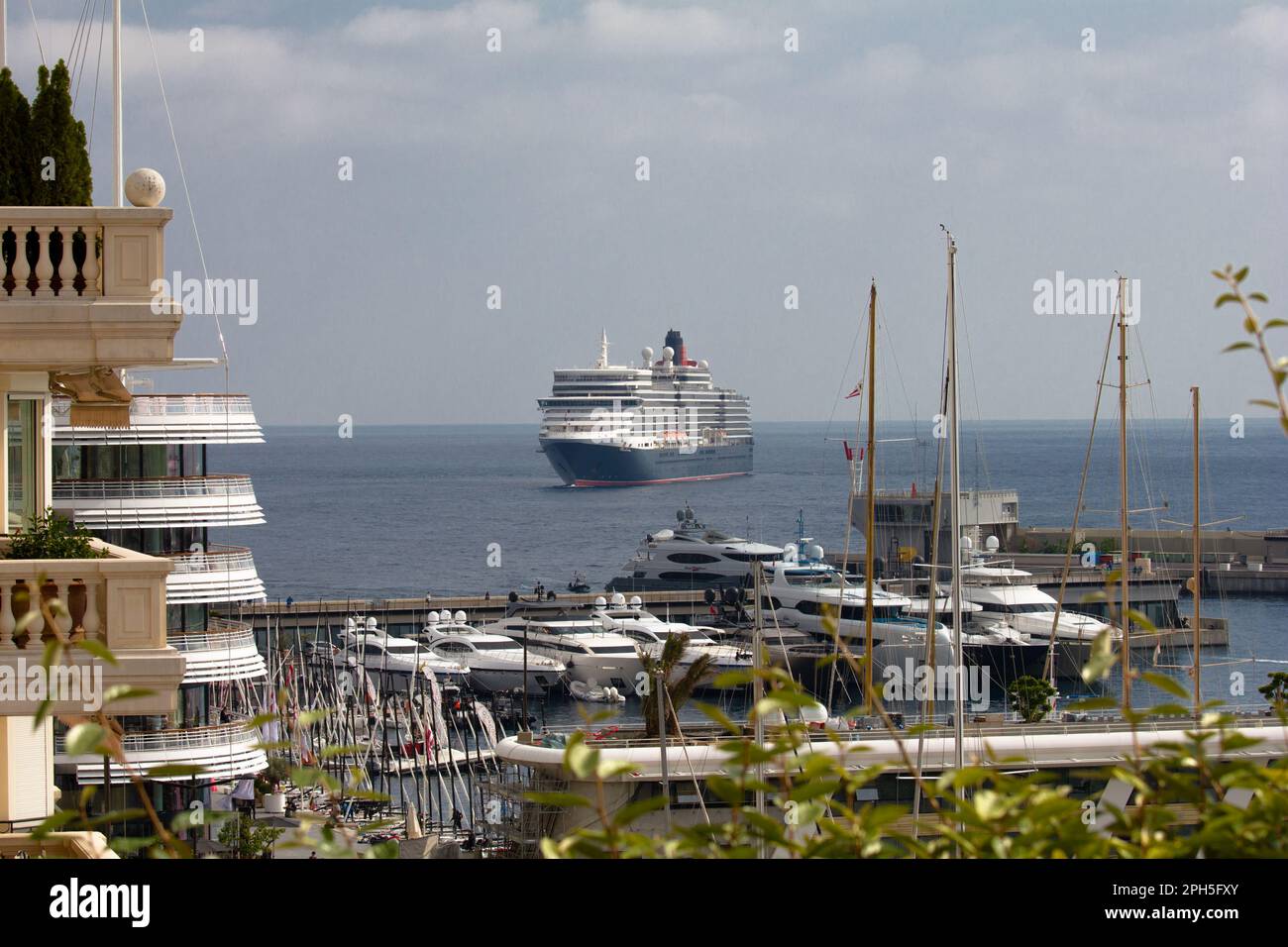 Le paquebot Cunard Queen Elizabeth est ancré au large de Monaco, Monte Carlo. Super yachts amarrés dans le port et une partie du Yacht Club de Monaco visible. Banque D'Images