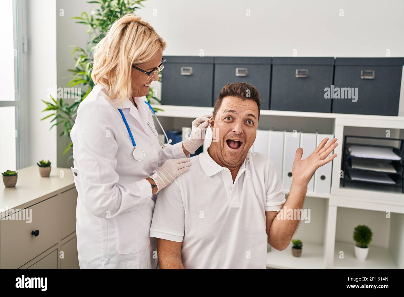 Homme hispanique ayant reçu une aide auditive médicale chez le médecin célébrant la victoire avec un sourire heureux et une expression gagnante avec des mains levées Banque D'Images