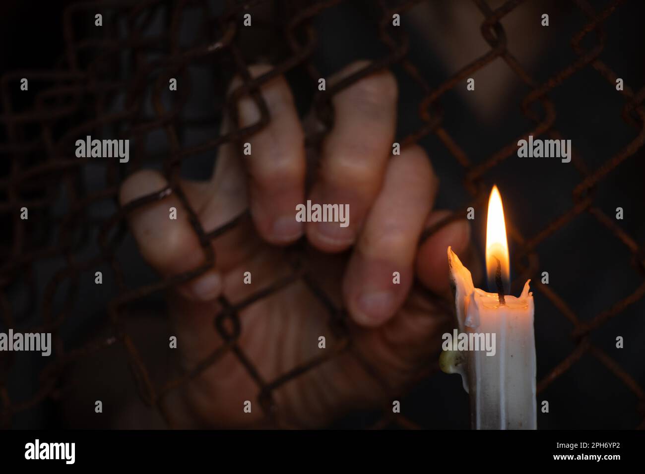 les vieilles mains de femmes pendent sur une clôture en maille de fer dans la serrure sur le fond d'une bougie en feu Banque D'Images